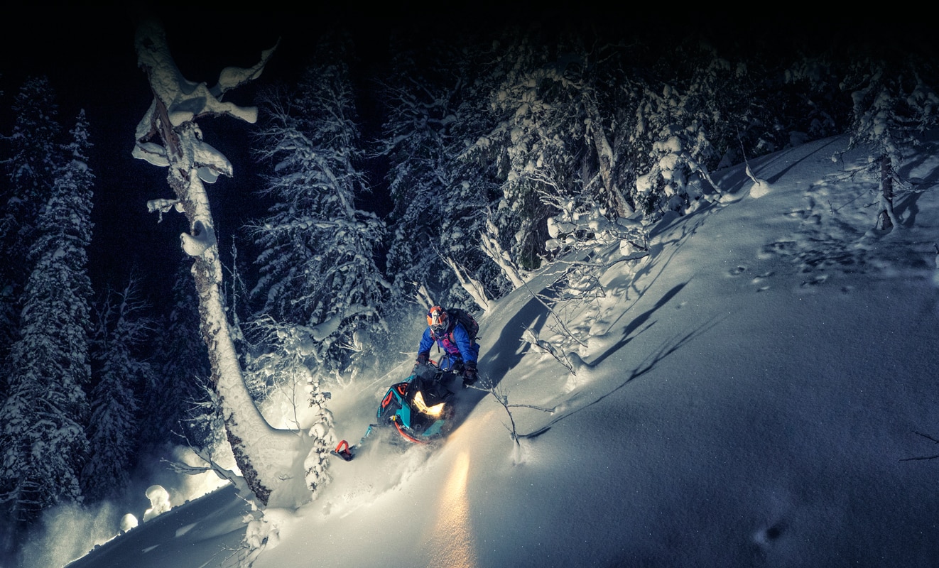 A man makes a tight turn on a snowy hill with his Lynx Boondocker 3900 Model during the night