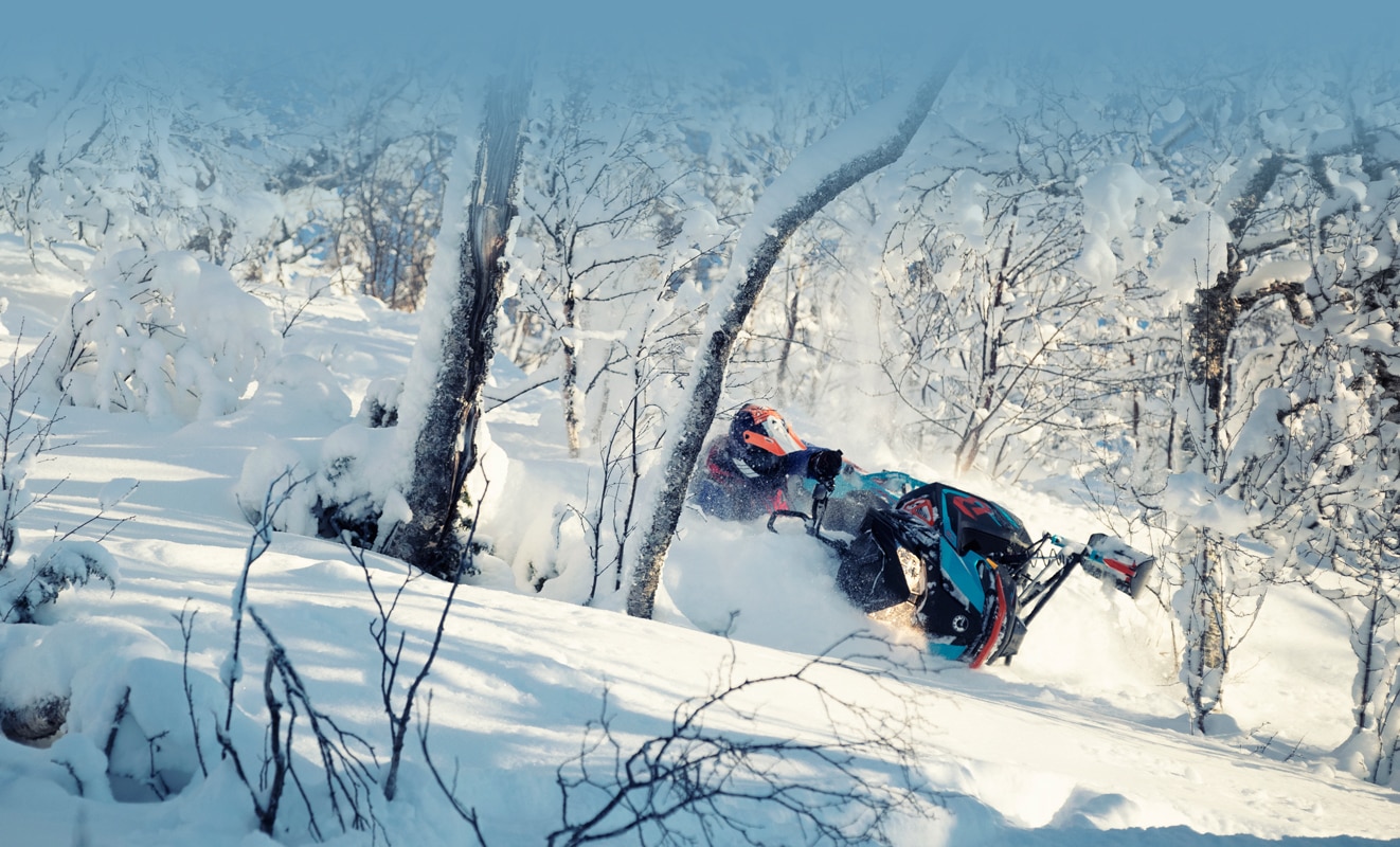 Muž projíždějící zasněženým lesemna sněžném skútru Lynx BoonDocker 3900 