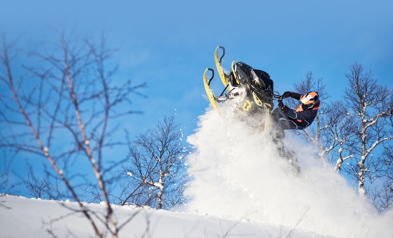 Muž skákající se svým sněžným skútrem Lynx BoonDocker 3900 v zasněženém lese