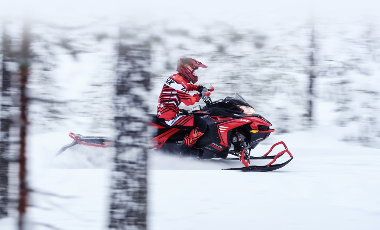 A man is riding at high speed throught the forest with his Lynx Rave Re Snowmobile Model 