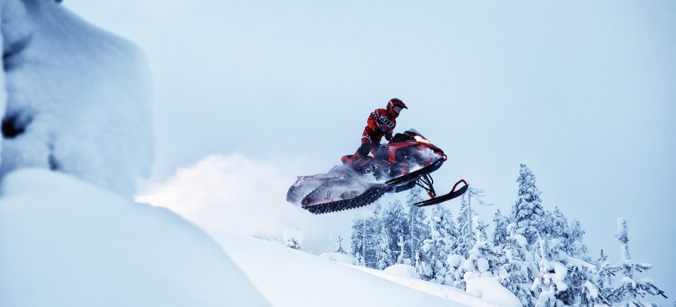 A man is jumping with his Lynx Rave Re Snowmobile Model the hill