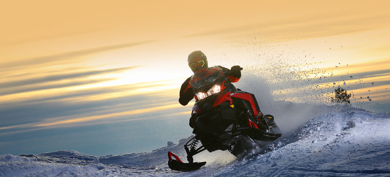 A man is riding his Lynx Rave Re Snowmobile Model at high speed during the sunset