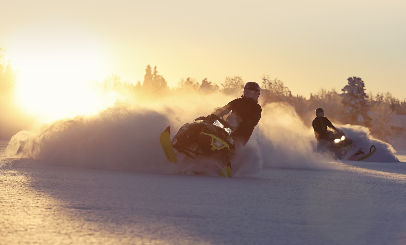 Dva muži driftující na sněhu se svými sněžnými skútry 