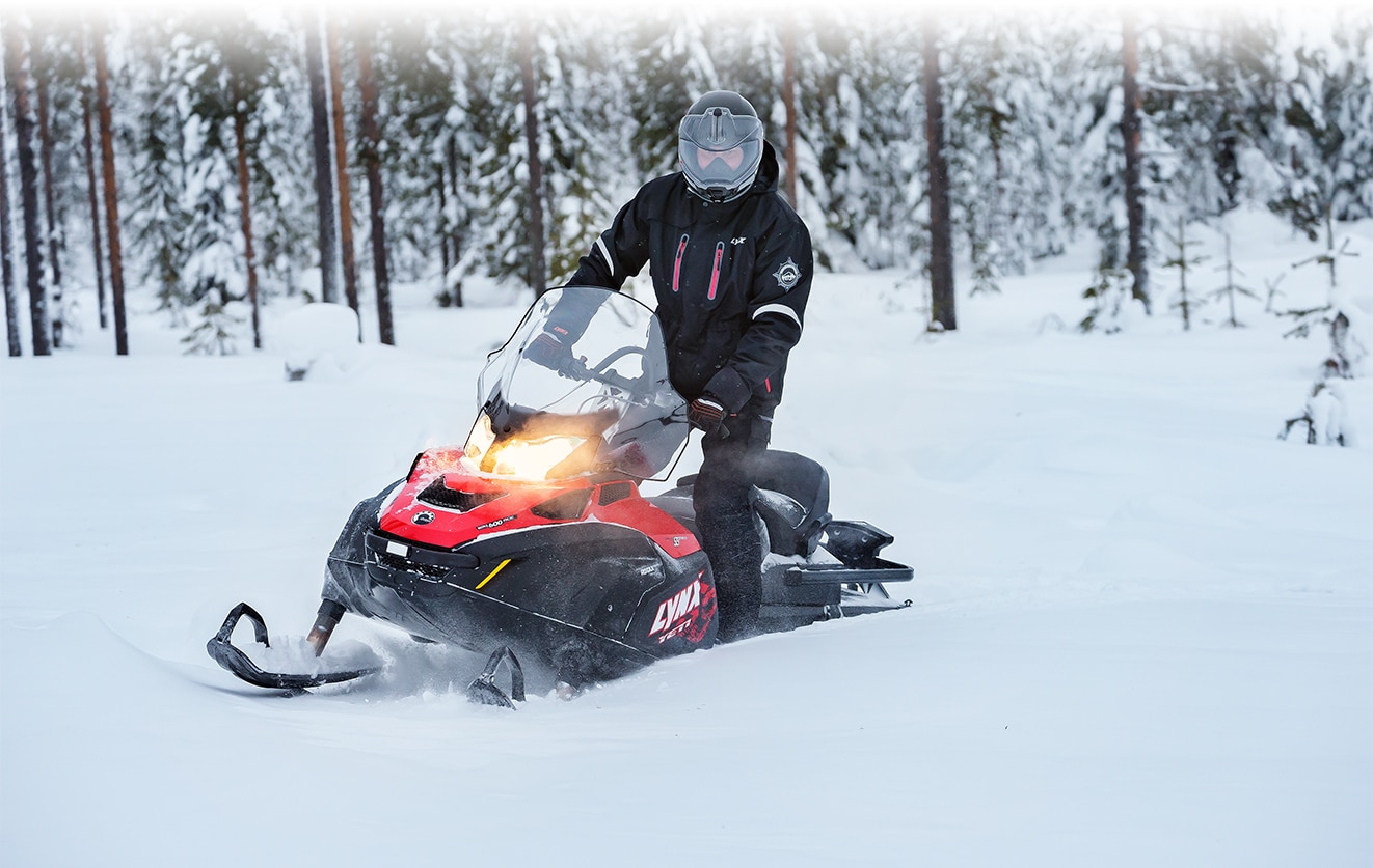 Muž stojící na stupačkách svého sněžného skútru 59 Ranger Yeti