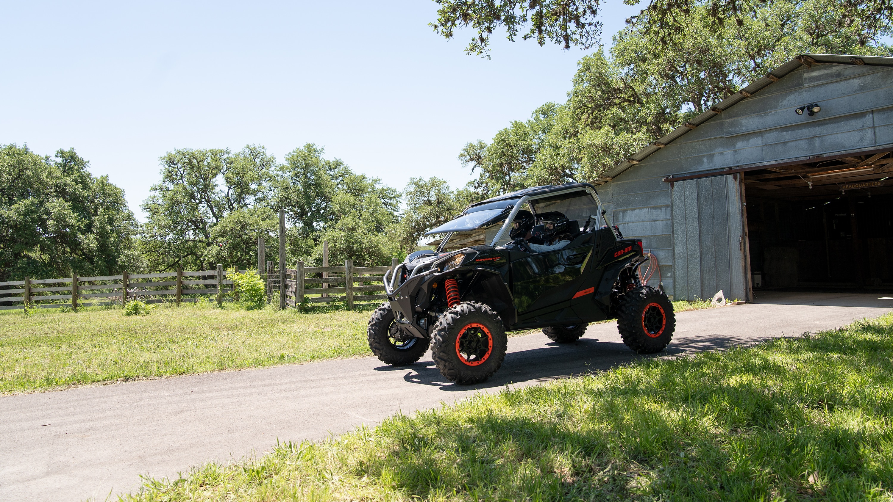 Two men riding a Maverick Sport near a barn