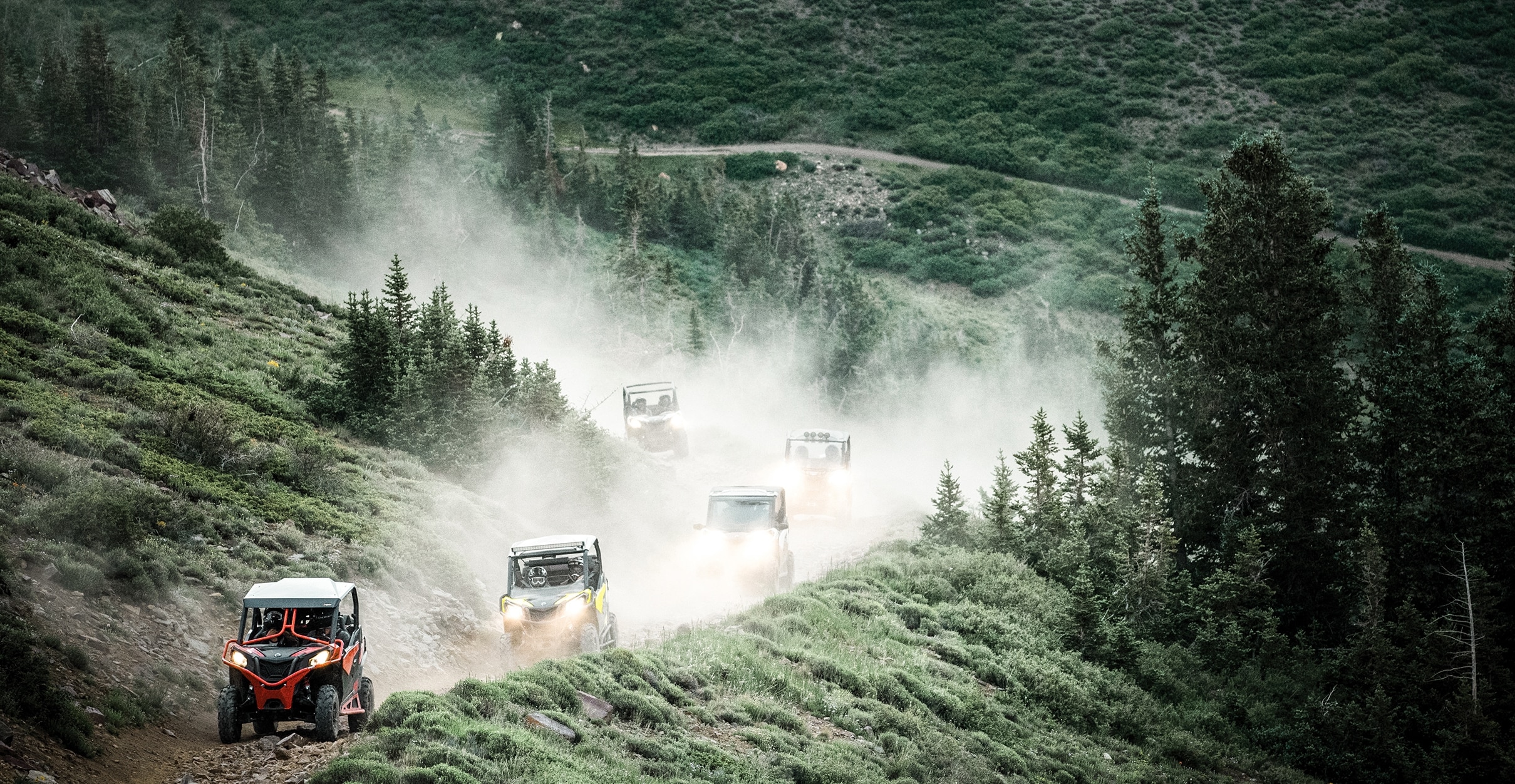 Päť terénnych vozidiel Maverick Trail jazdí po lesnej ceste v horách.