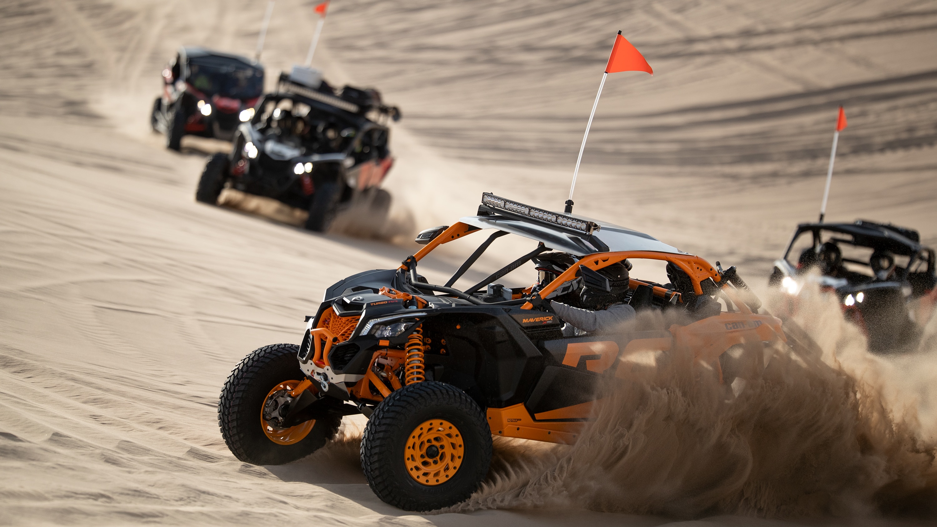 Four Maverick side-by-side drifting through sand