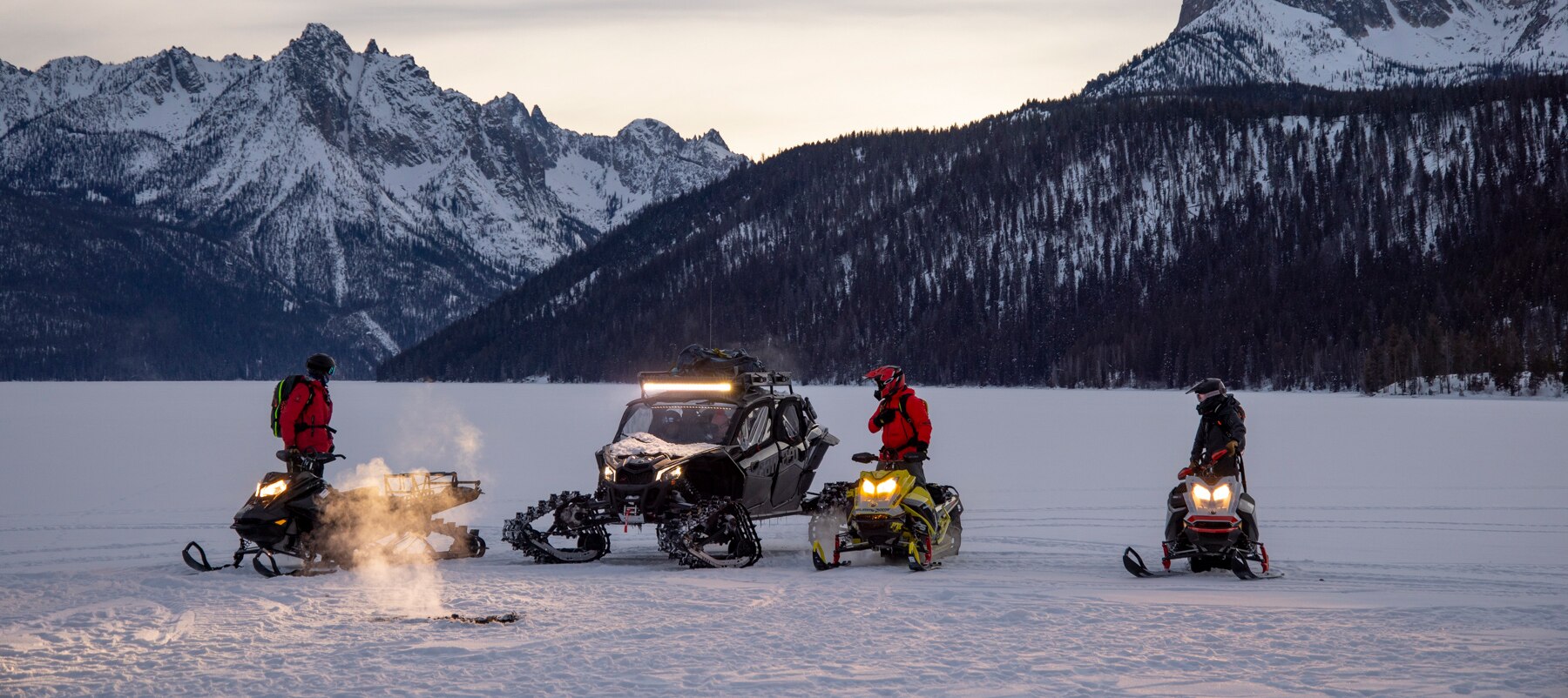 3 men riding ski-doo with a sunset