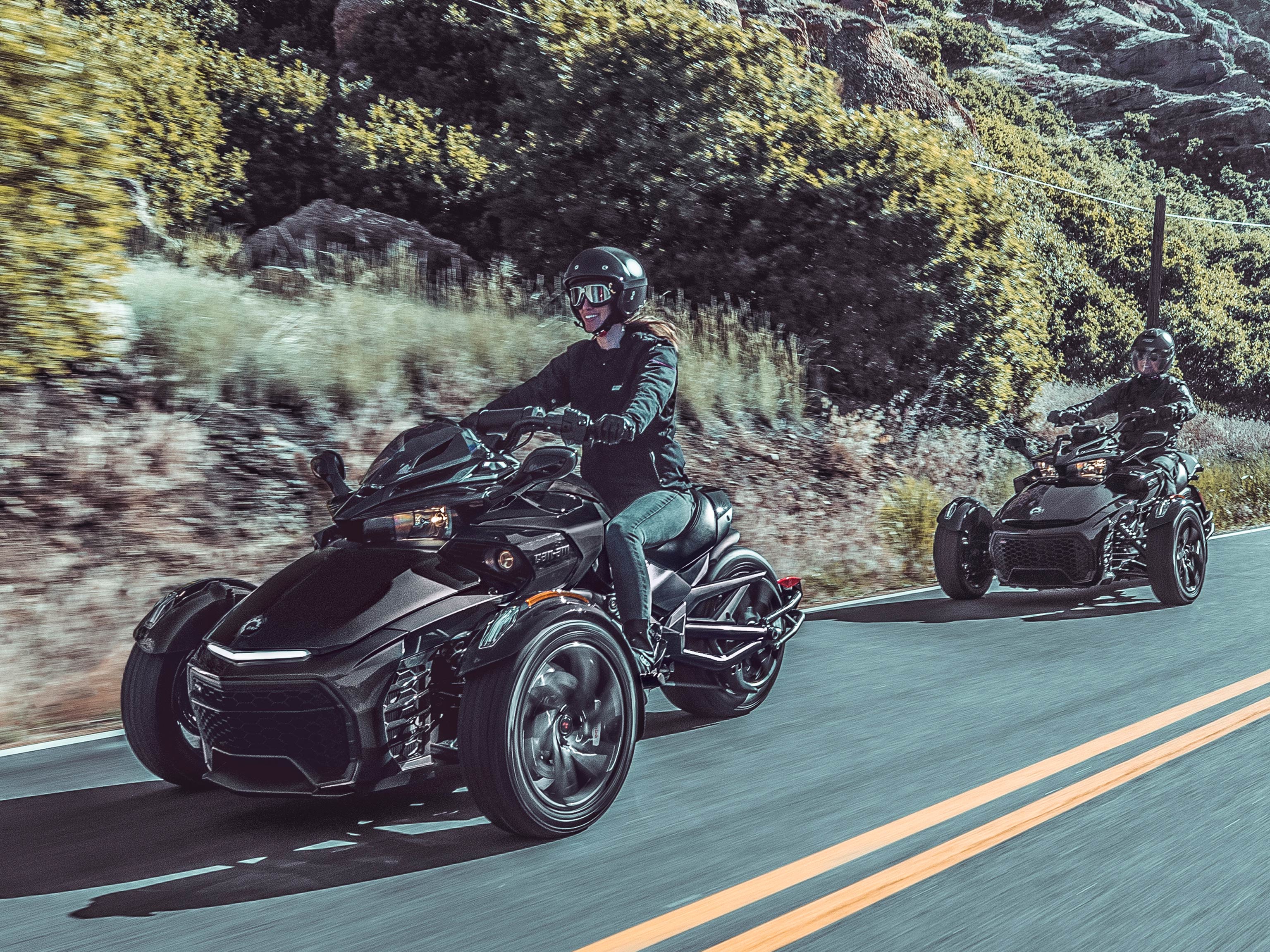 Two people riding Can-Am Spyder vehicles along an open desert road