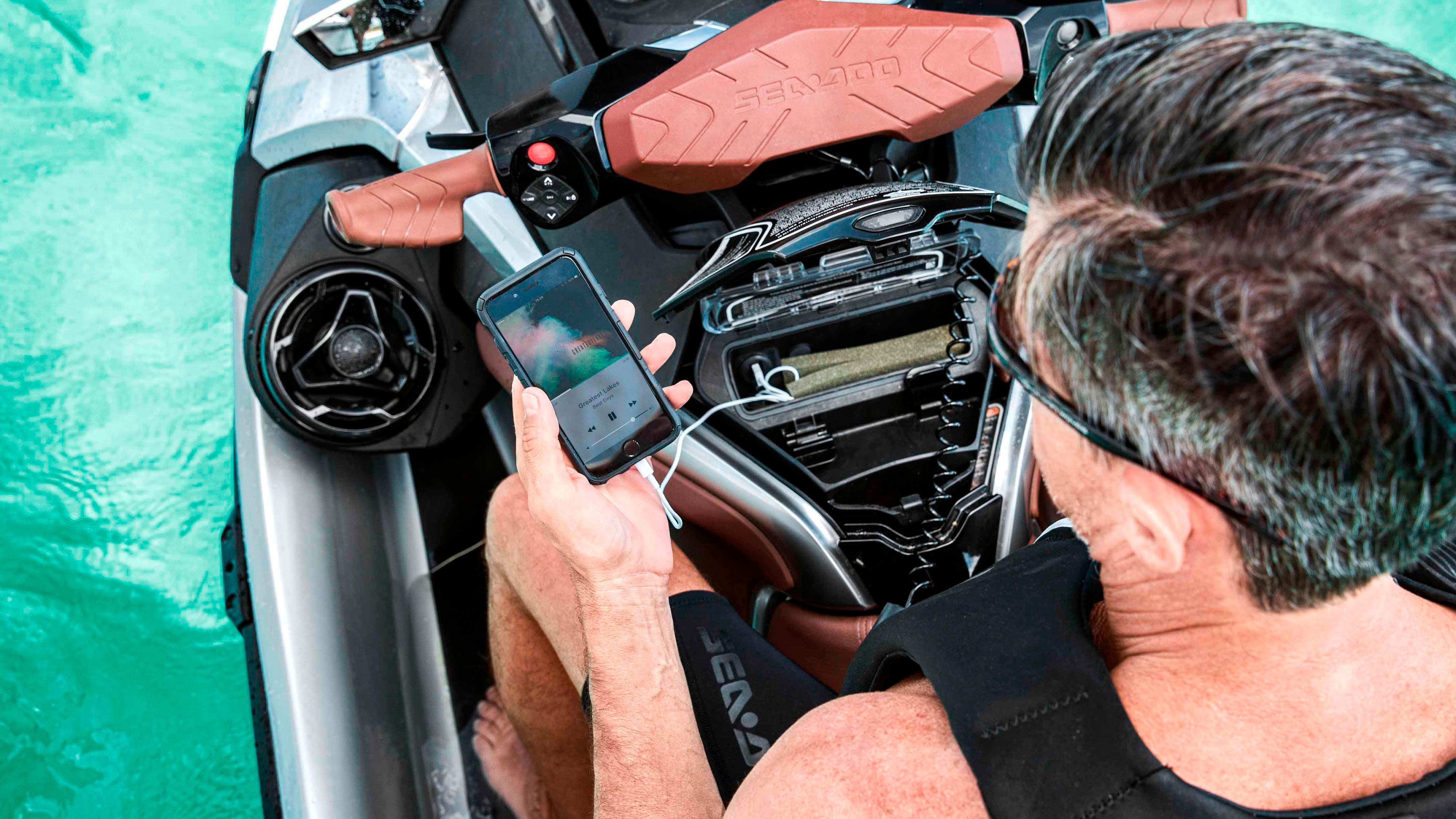 Man changing music with his phone sitting on a Sea-Doo GTX