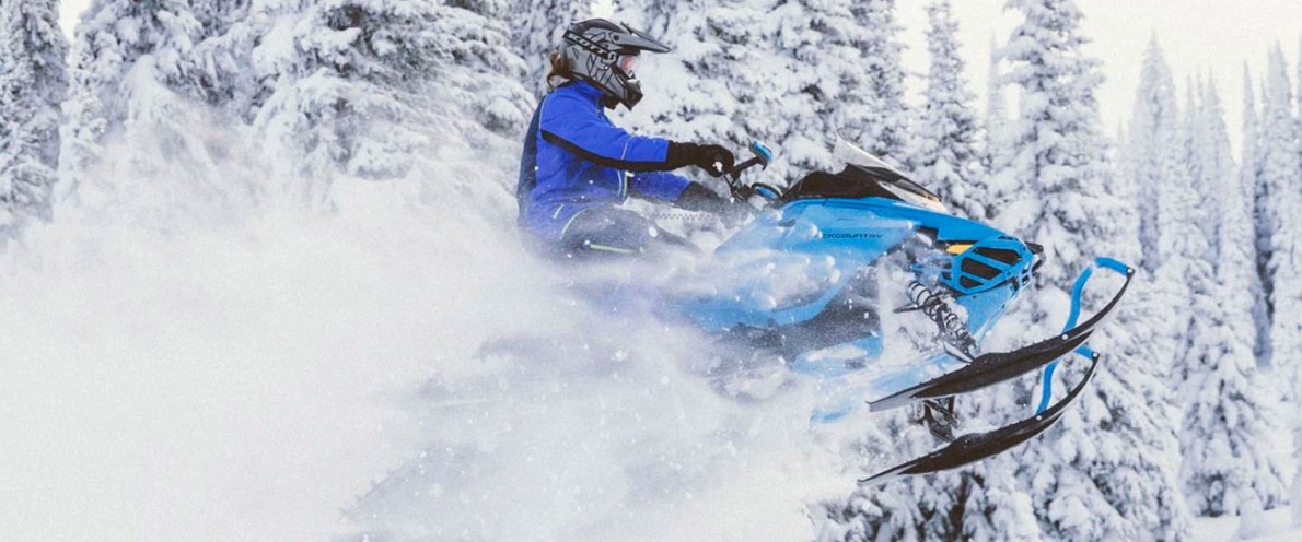Čovjek koji skače kroz snijeg svojim motornim sanjkama Renegade