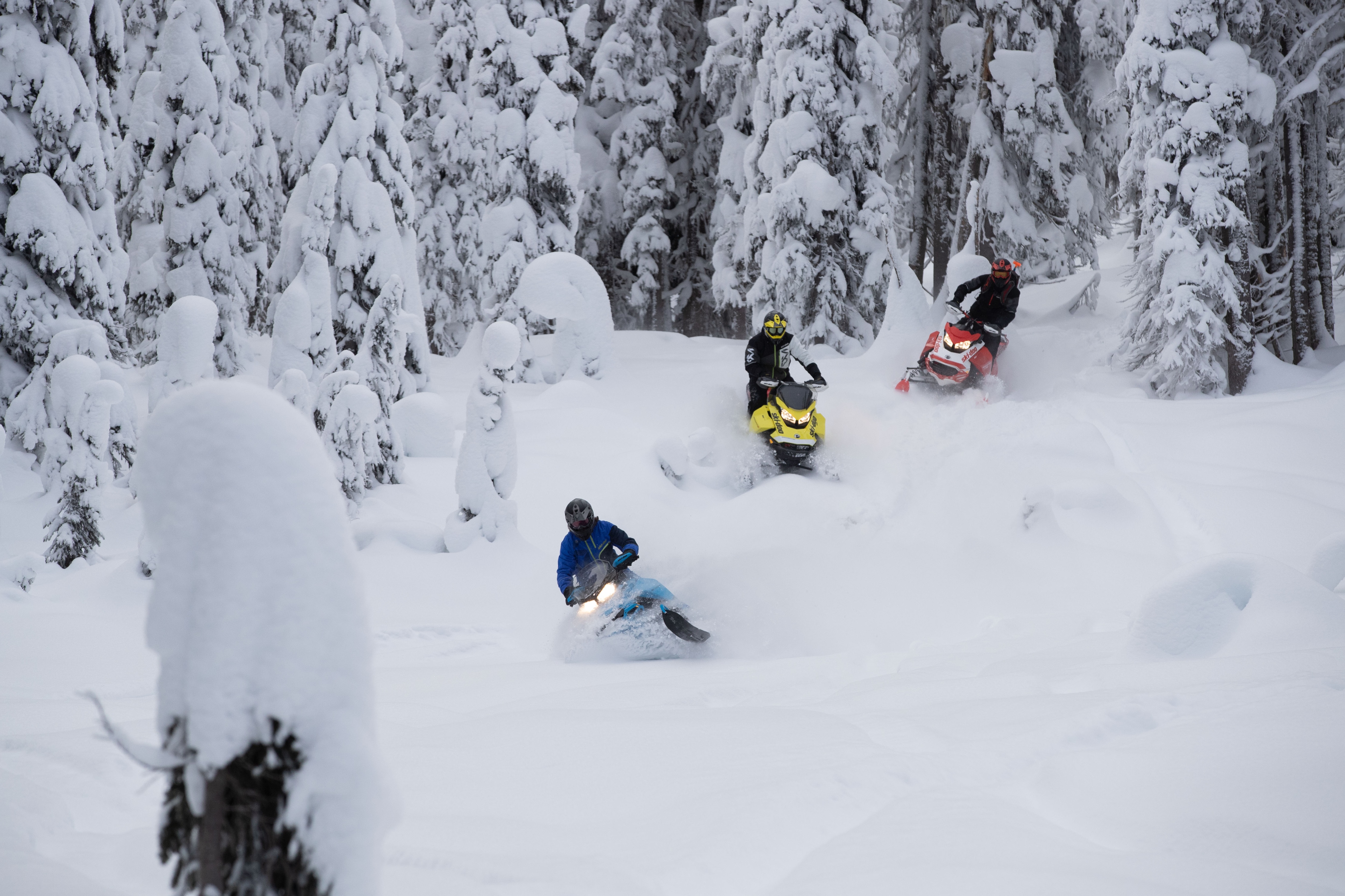 Tři přátelé jedoucí na sněžném skútru Ski-Doo hlubokým sněhem