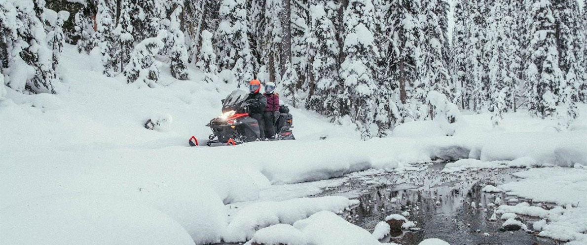 Pár jedoucí na sněžném skútru Expedition kolem zamrzlé vodní plochy