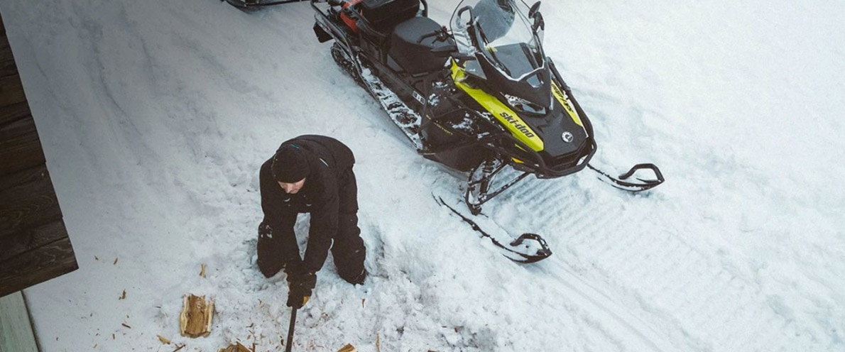  Čovjek koji cijepa drva u blizini svoje motorne sanke Expedition