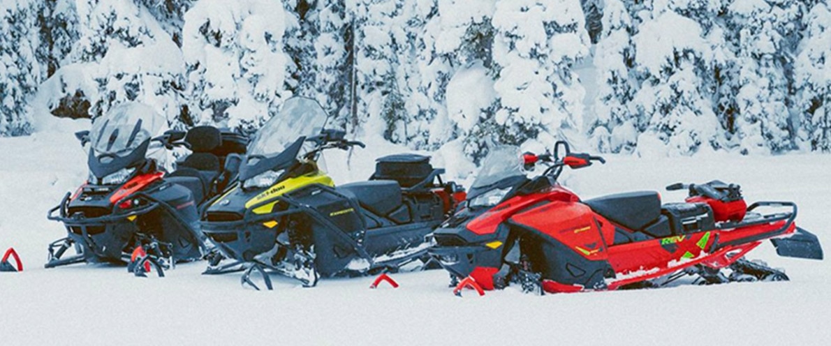 Three snowmobiles parked in a snowy trail