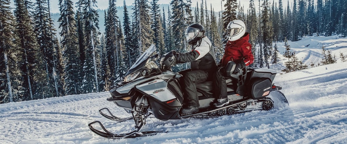Muž a žena jedoucí sněhem na sněžném skútru a Ski-Doo Grand Touring