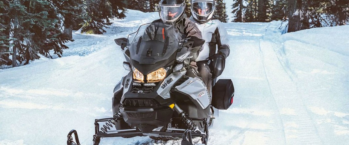 Man and woman driving through snowy forest trail on a Grand Touring