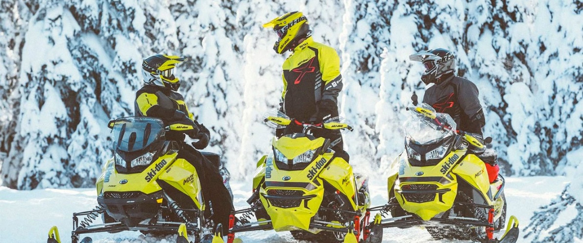 Tři přátelé sedící na sněžném skútru Ski-Doo MXZ