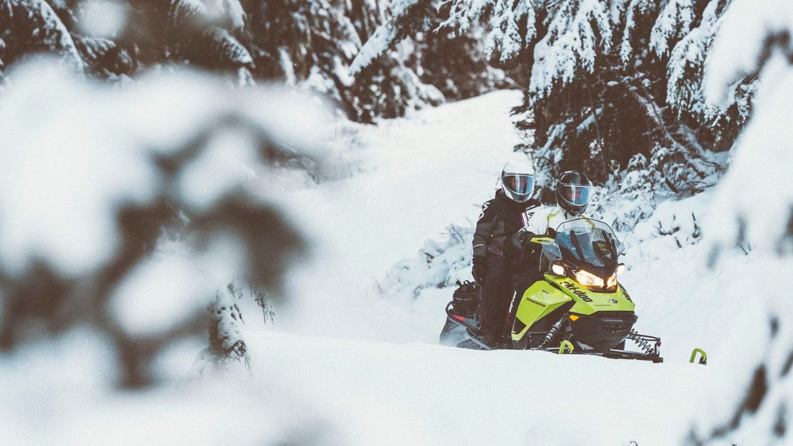 Two friends driving a Ski-Doo through a snowy trail