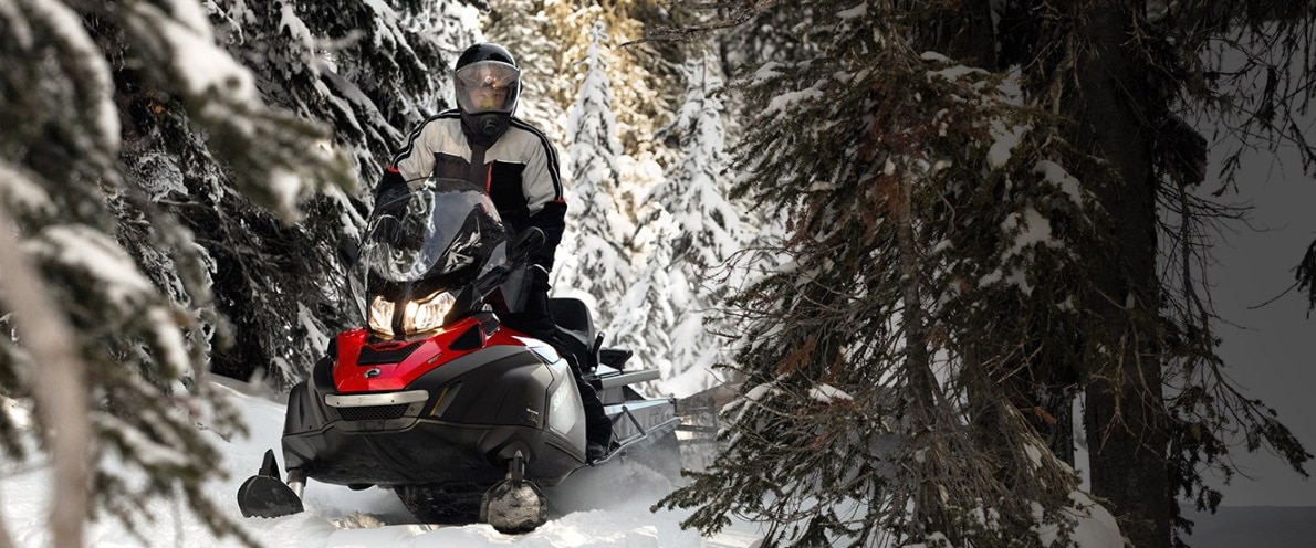 Man driving Skandic snowmobile through snowy forest