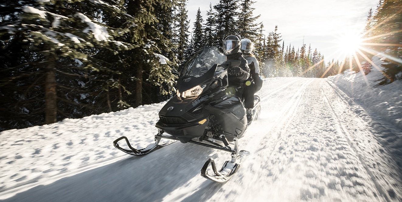 A man and woman riding a Ski-Doo Grand Touring through a forest trail
