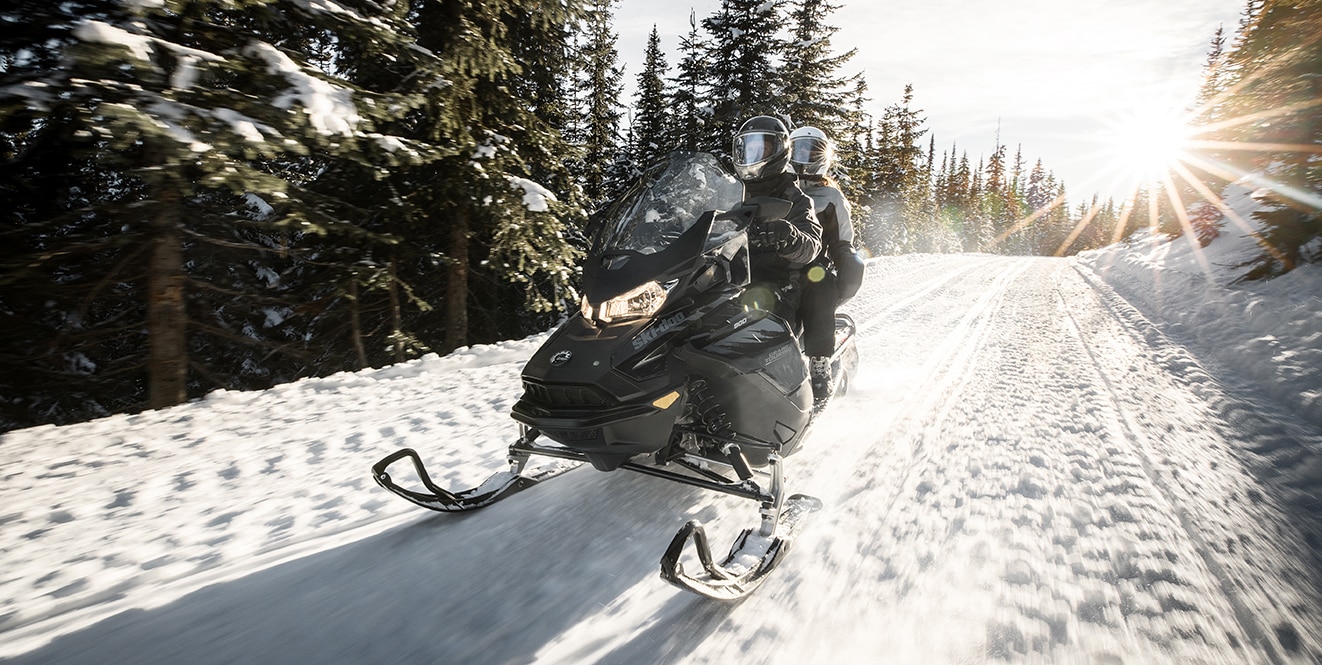 Egy férfi és nő hószánozik a Ski-Doo Grand Touring egy erdei ösvényen