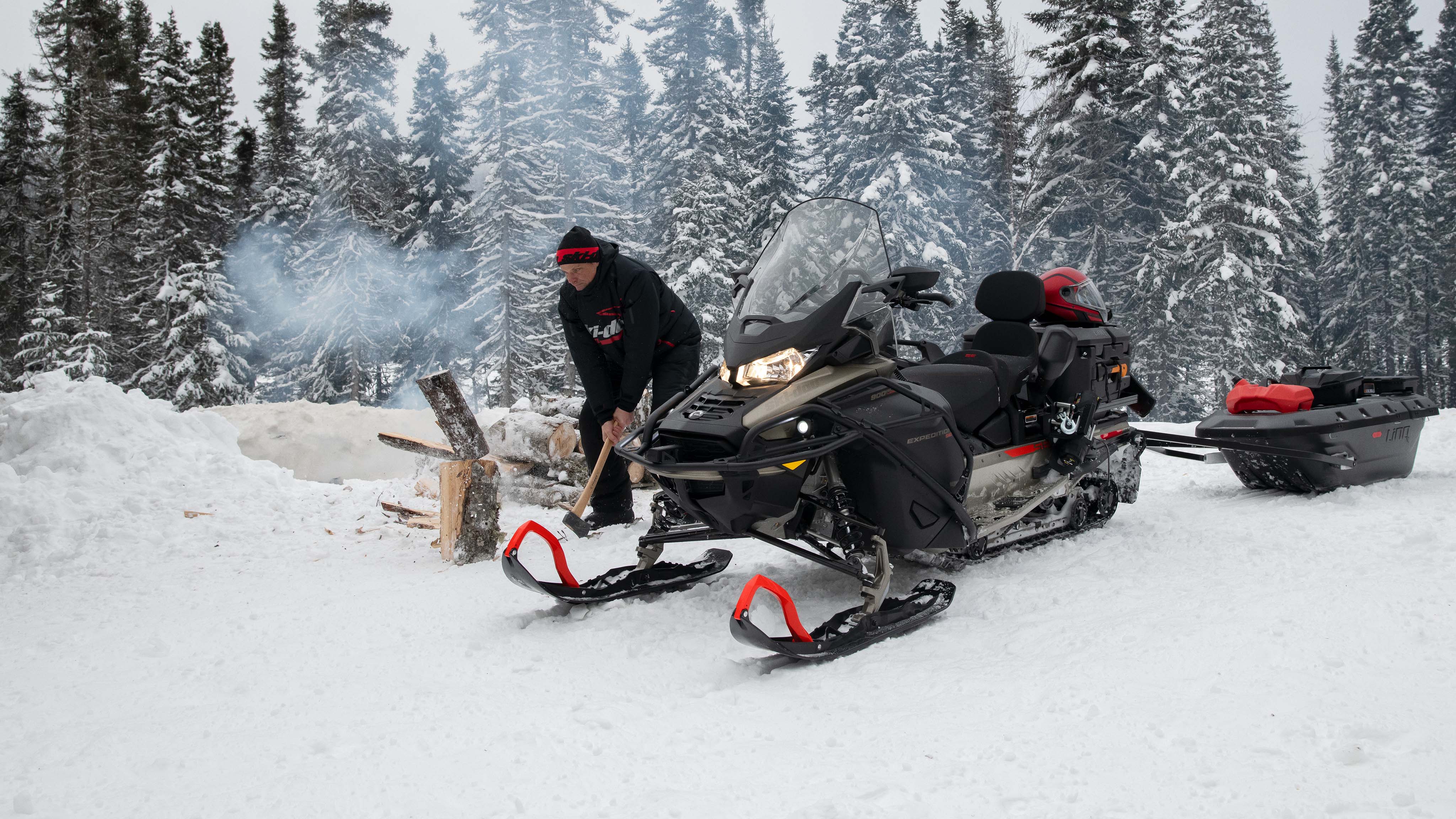 Man chopping firewood beside Ski-doo