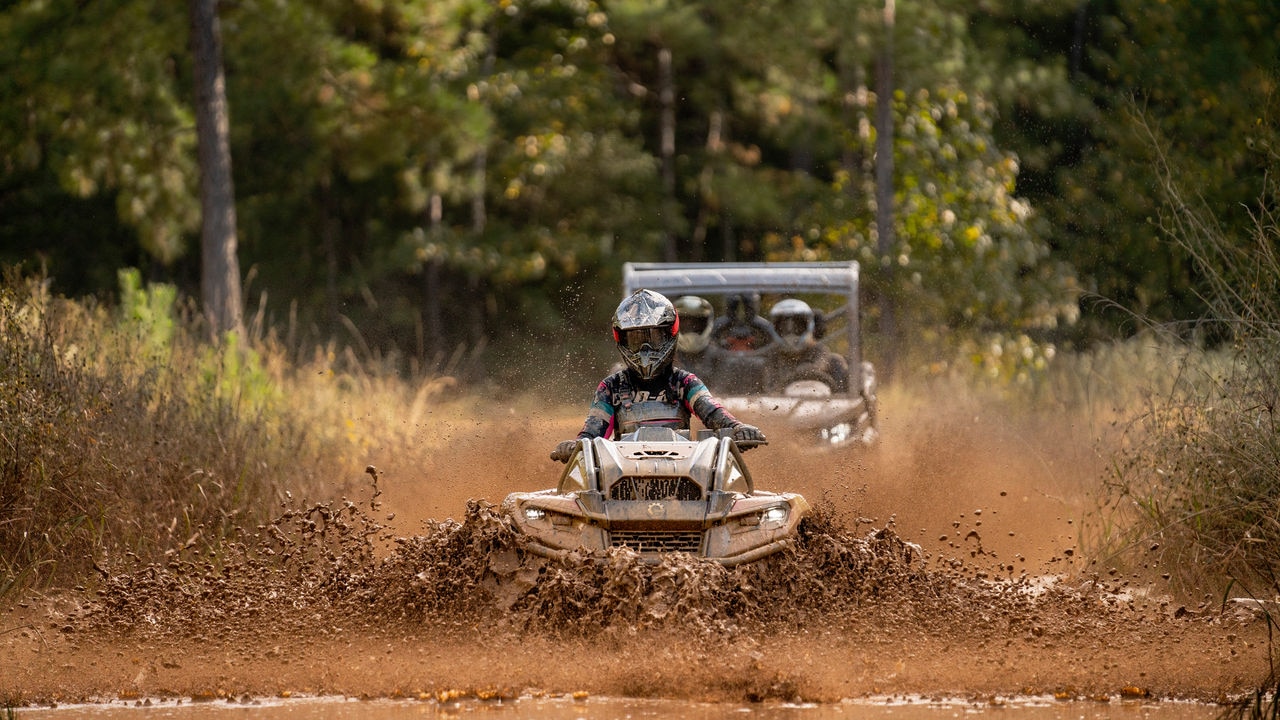An ATV and a side-by-side driving down a trail, throwing mud