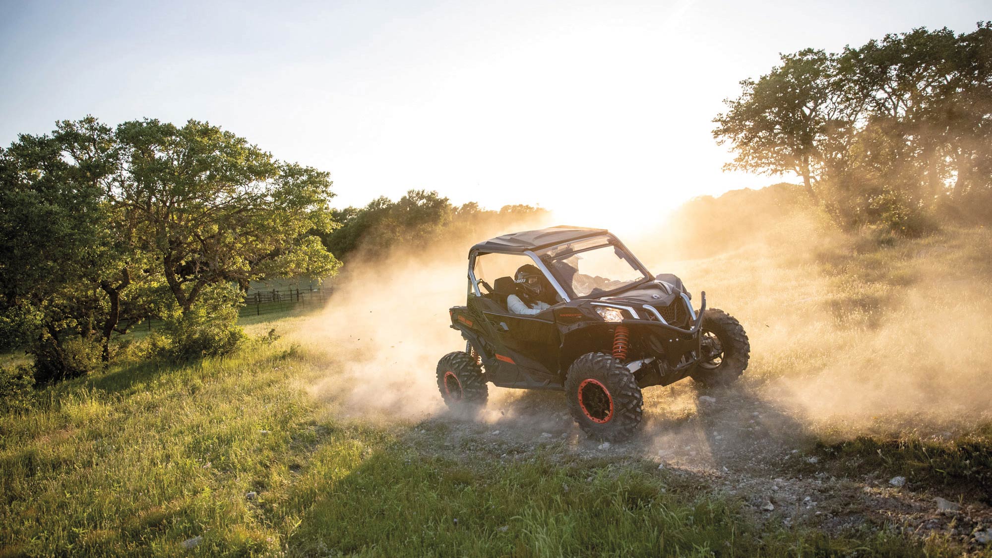 A Can-Am Maverick Sport X 1000r rolling down a slope with dust in the air