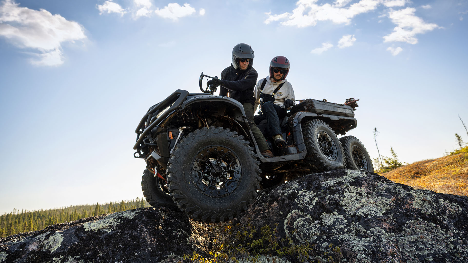 Two riders driving over a rock in their 2026 Can-Am Outlander Max 6x6