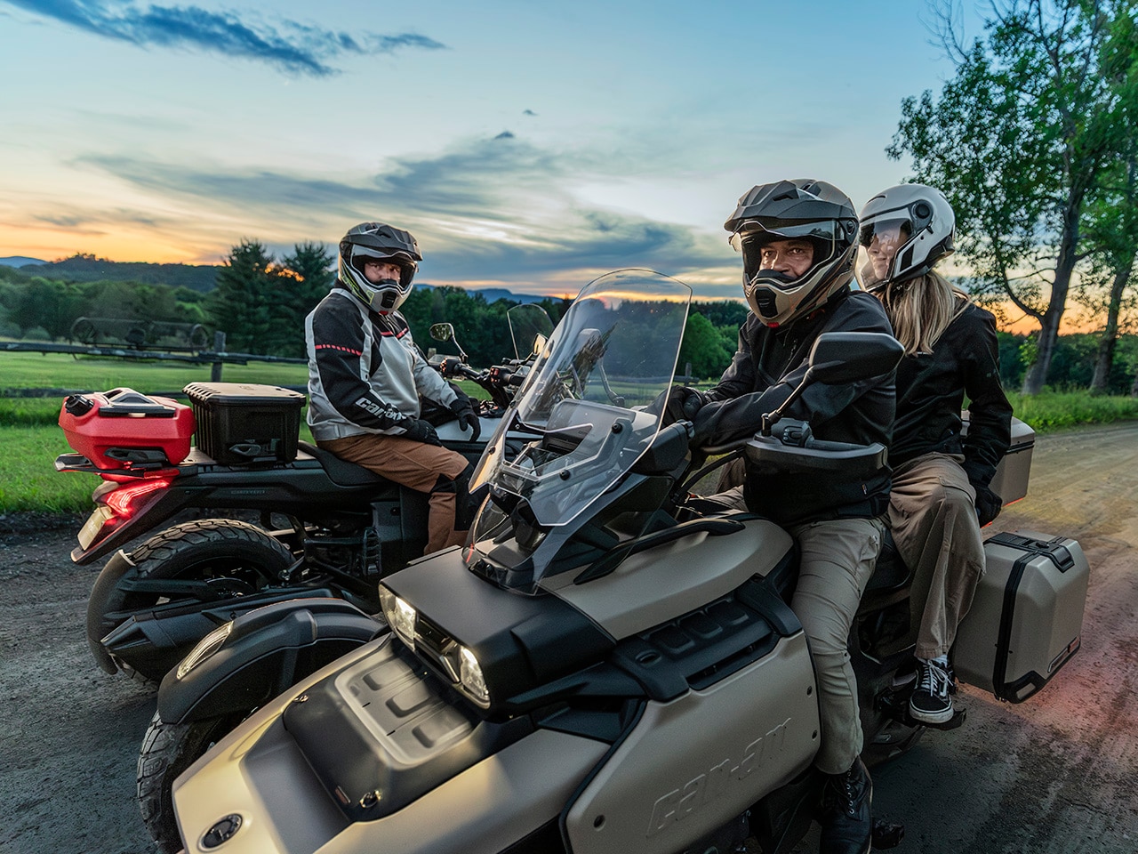 Three friends sitting on Can-Am 3-wheel motorcycles next to a field