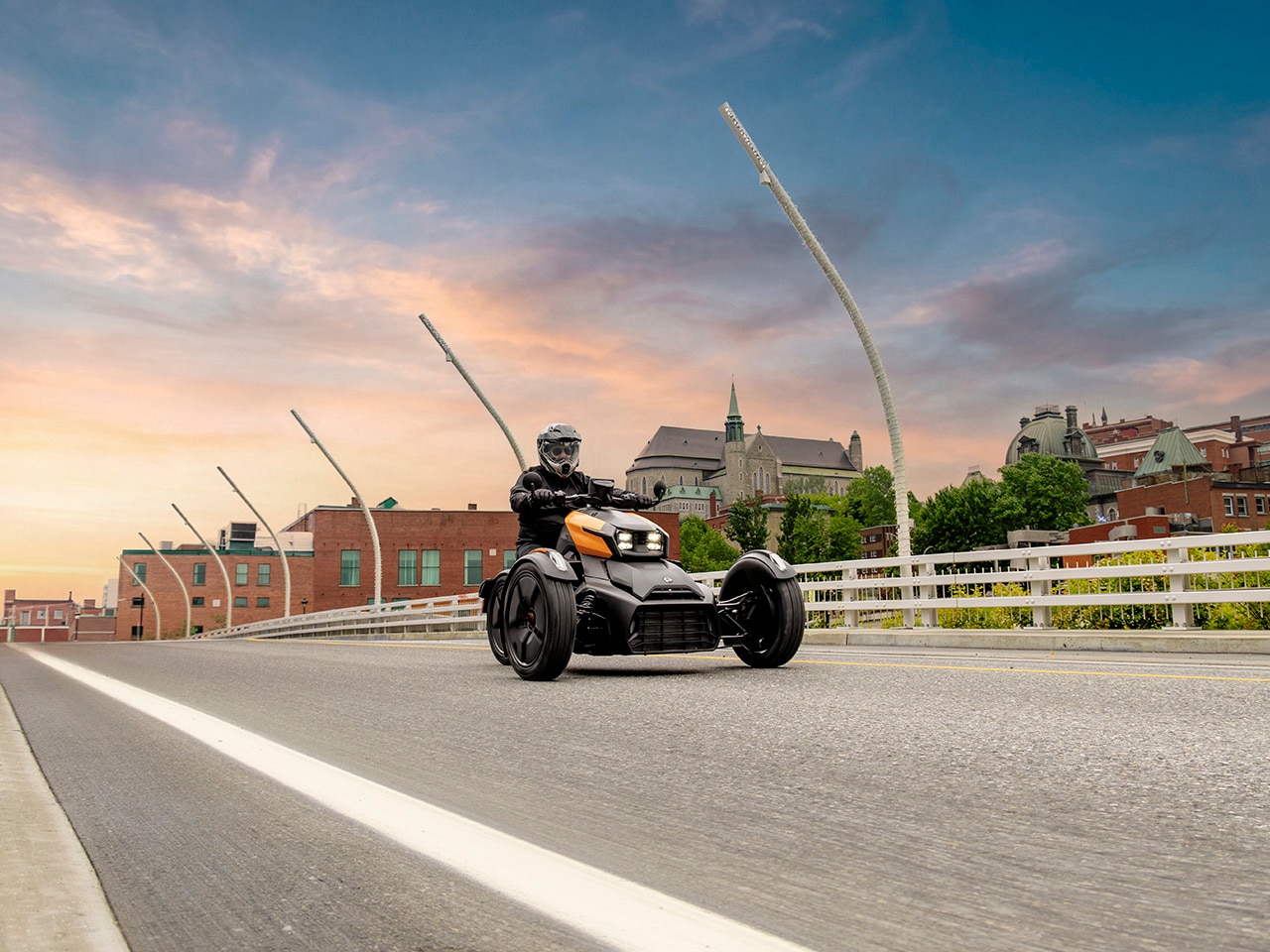 A 2027 Can-Am Ryker riding on a bridge with a city skyline in the background