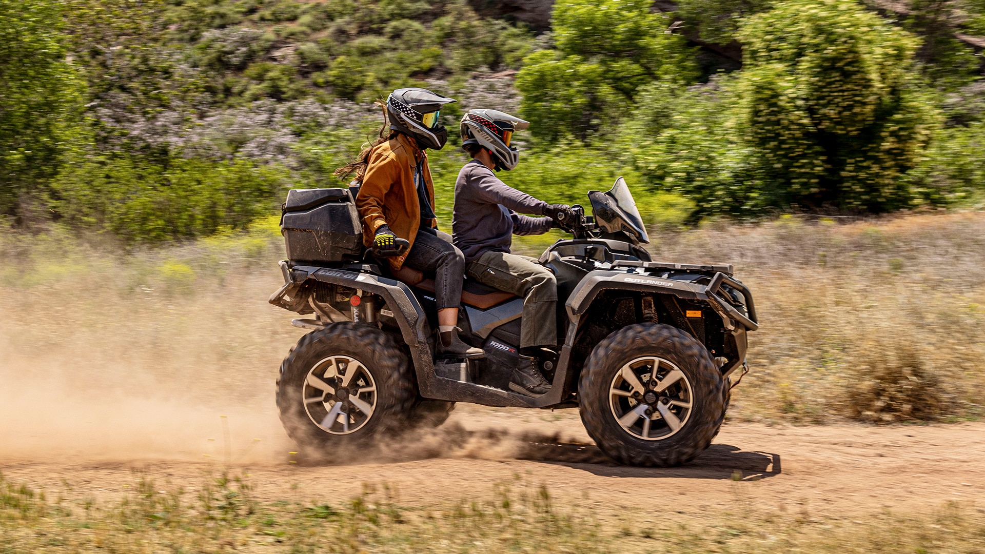 Two women riding on a Can-Am Outlander ATV on a dirt road