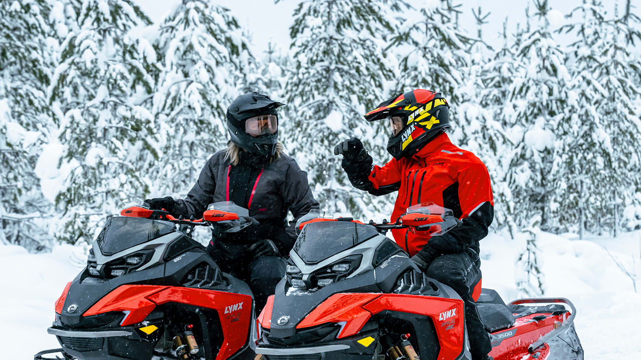 Man and woman chatting on Rave RE snowmobiles