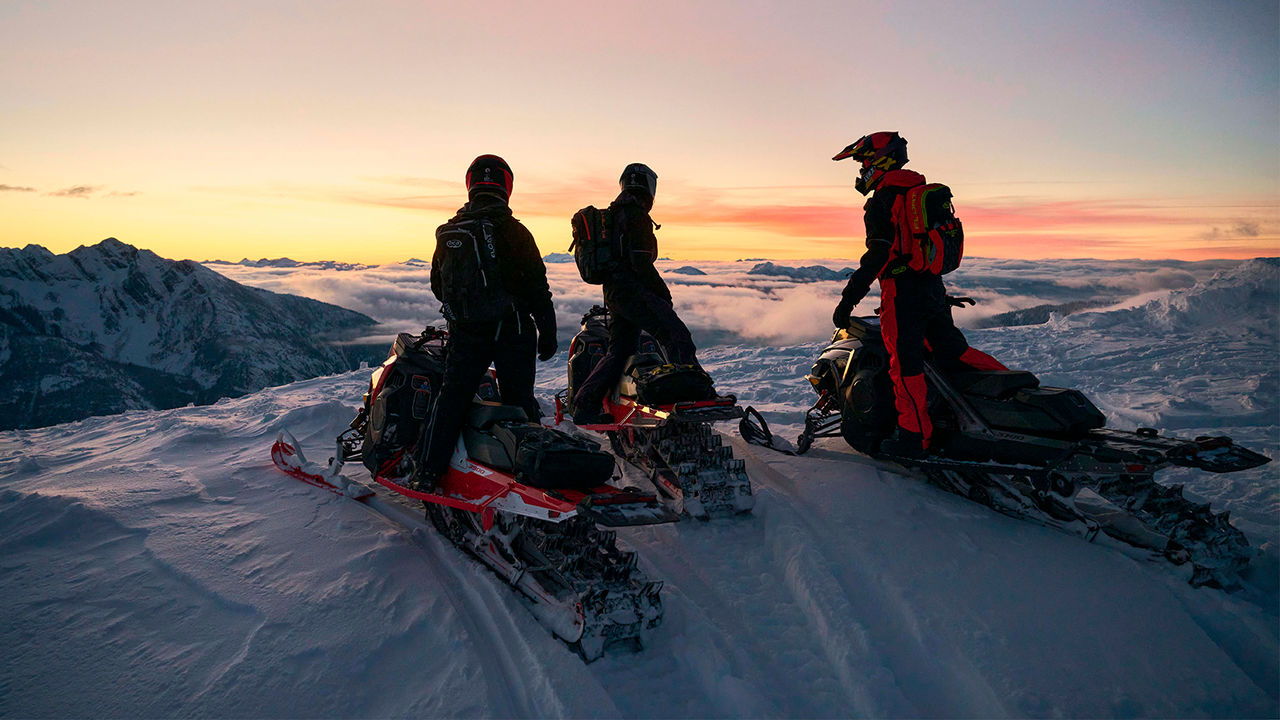 Three Lynx Shredder snowmobiles parking on top of the mountain at sunset