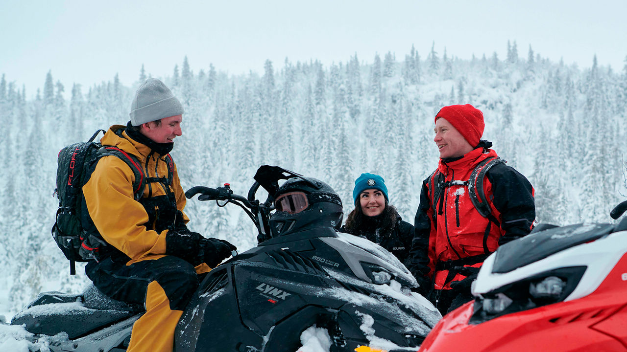 Three friends chatting and laughing on Lynx Shredder snowmobiles