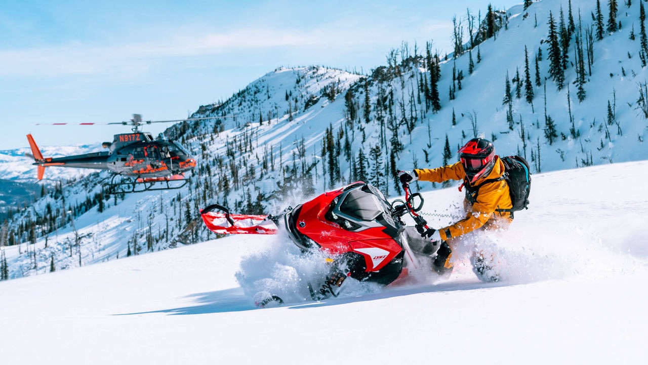 Ross Robinson conduisant une motoneige Lynx avec un hélicoptère en arrière-plan