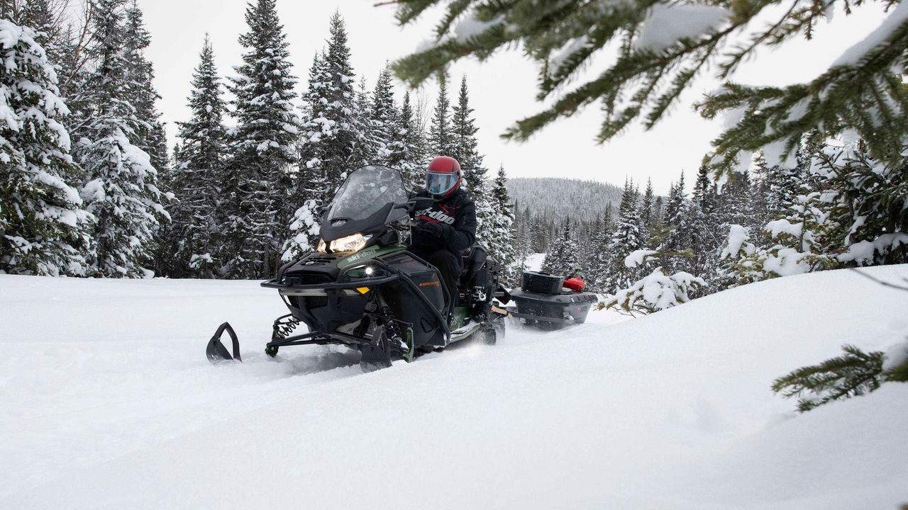 Muž ťahá vybavenie na saniach za skútrom Ski-Doo