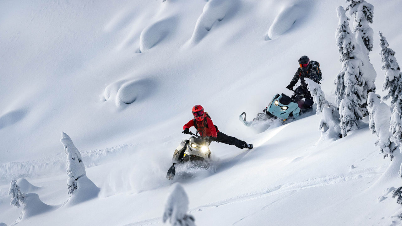 Dağda Ski-Doo bol kar motosikletini kullanan iki sürücü