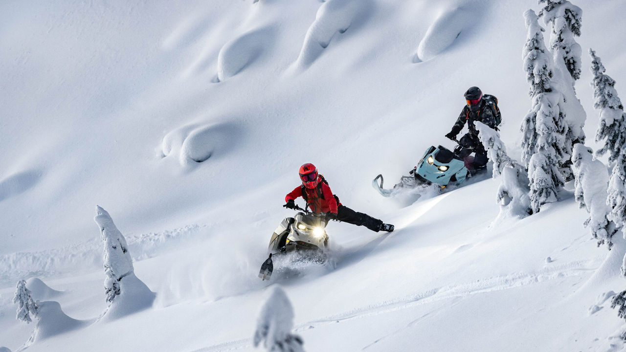 Двајца возачи на своите Ski-Doo моторни санки кои се спуштаат долж планината