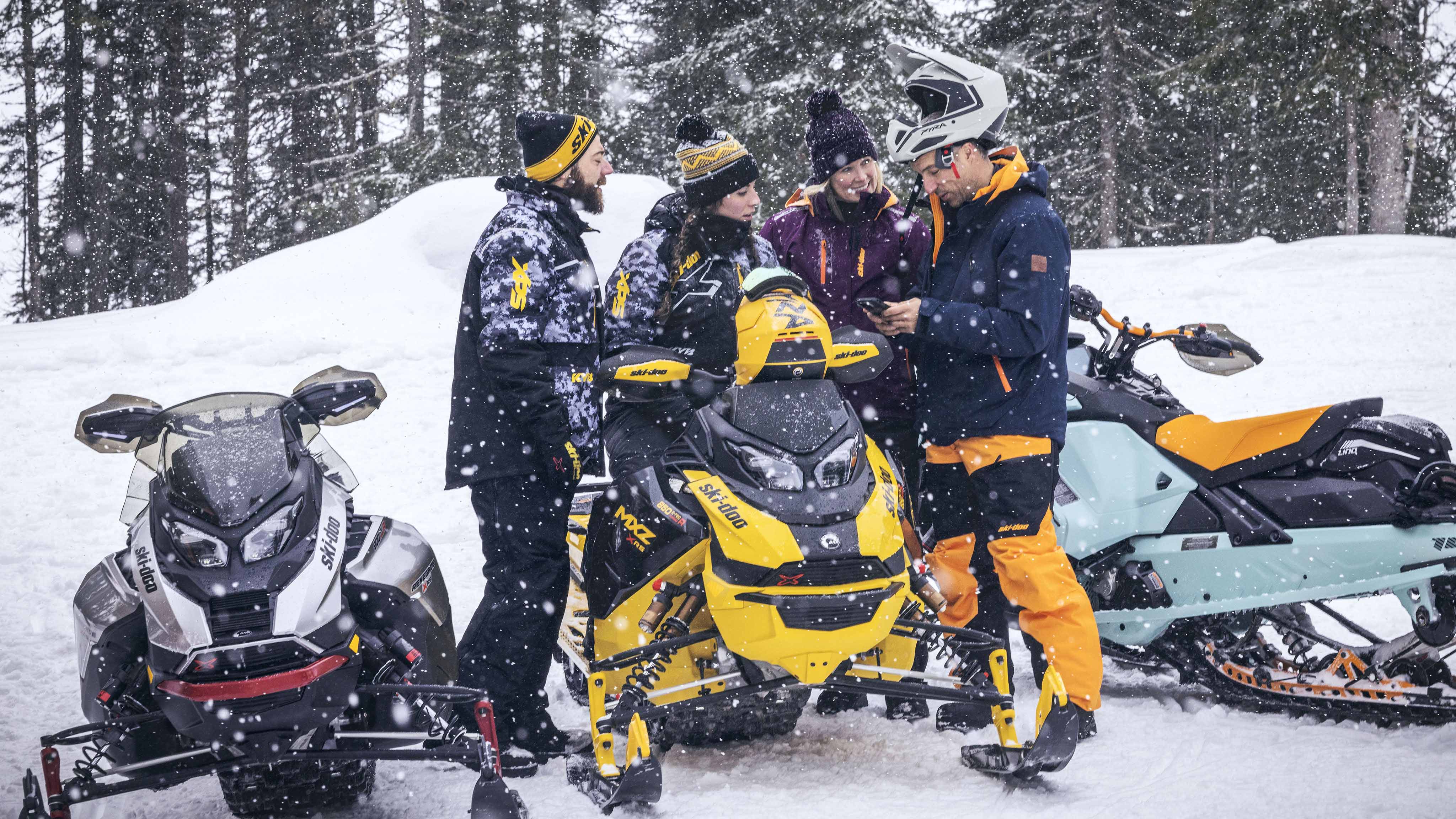 Group of snowmobilers looking at a cellphone next to their sleds