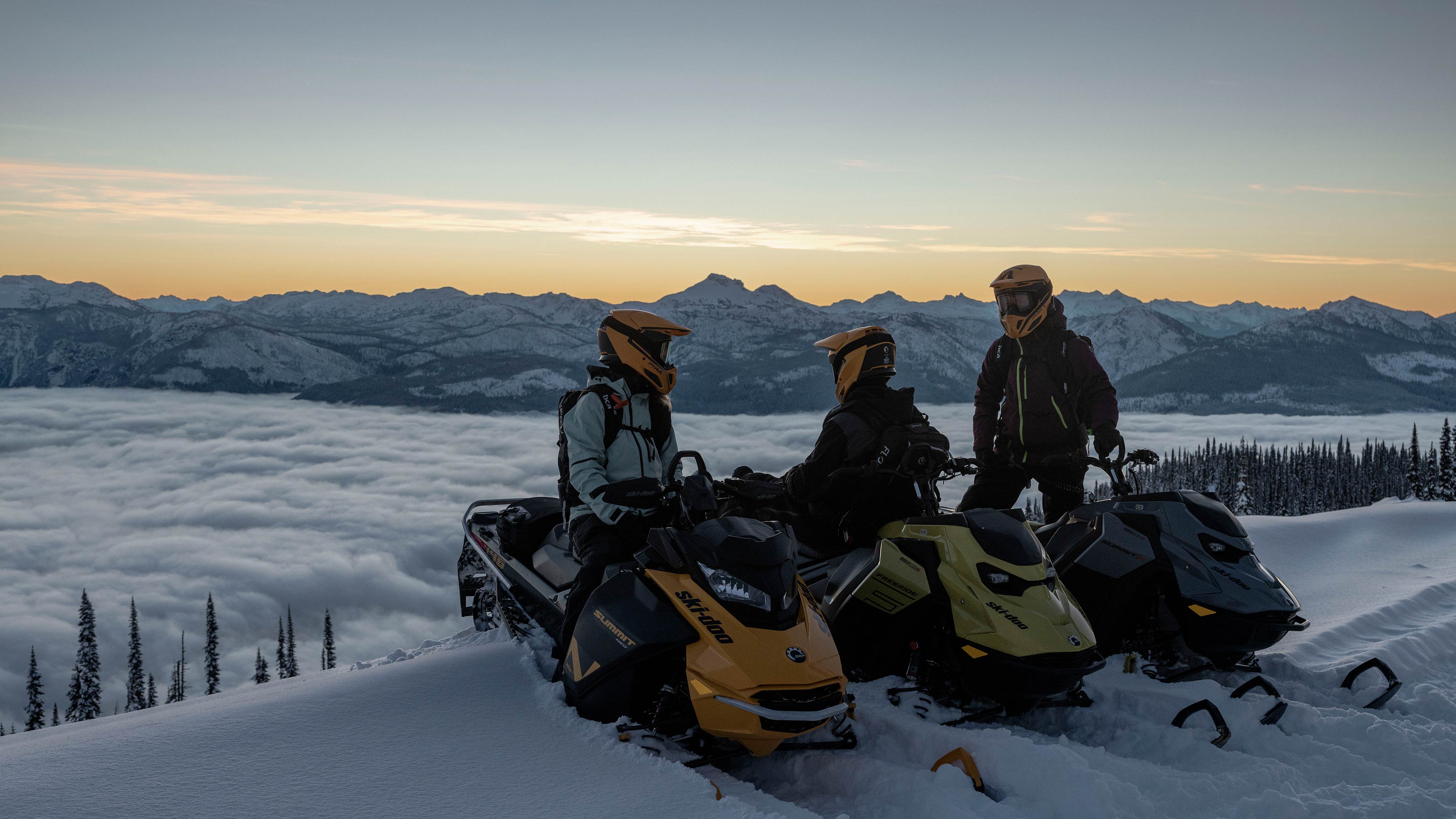 Traja jazdci Ski-Doo na ich skútroch na vrchole kopca