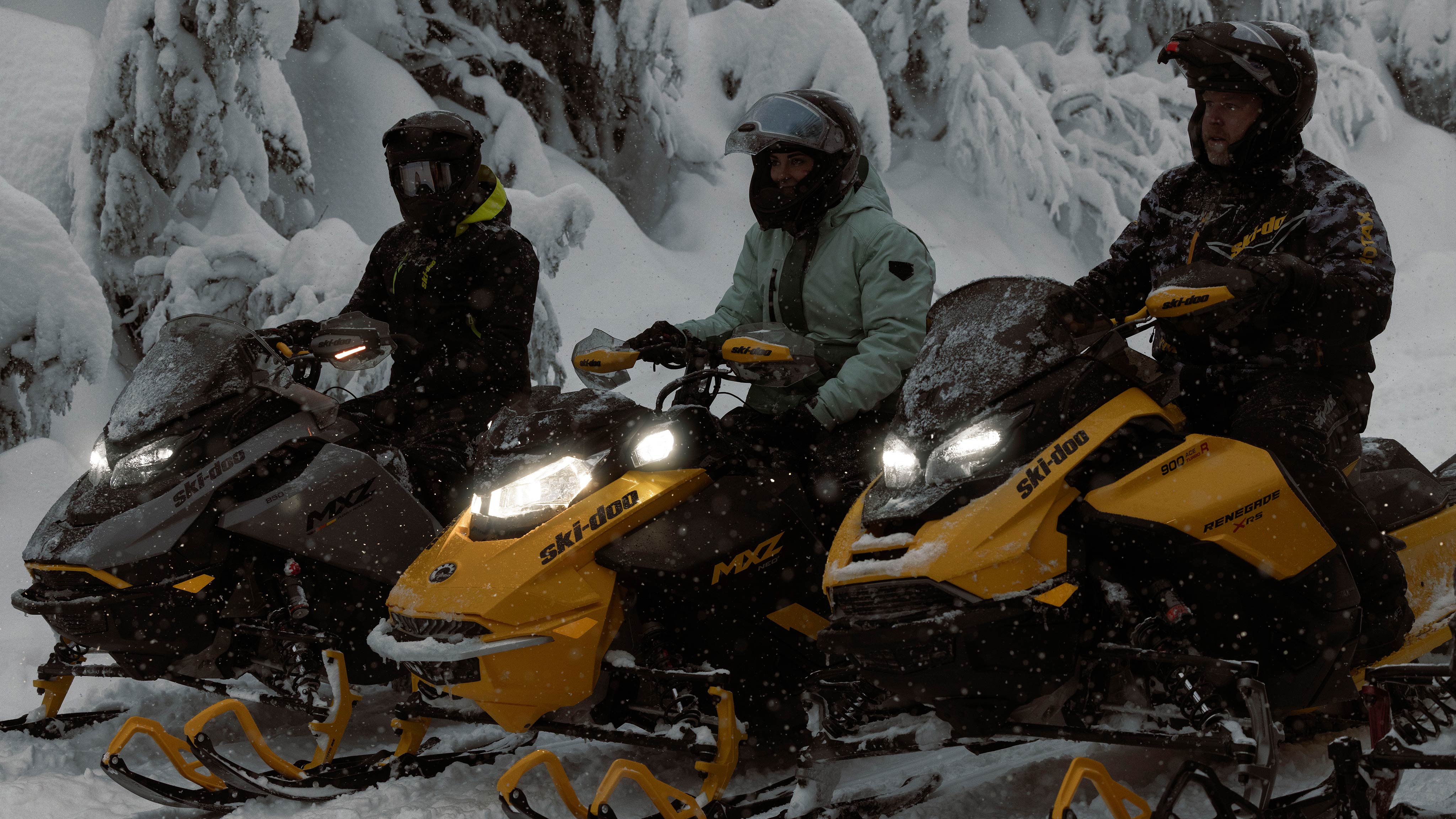 Trojica vozača koji se odmaraju od snježne vožnje na svojim Ski-Doo motornim sanjkama