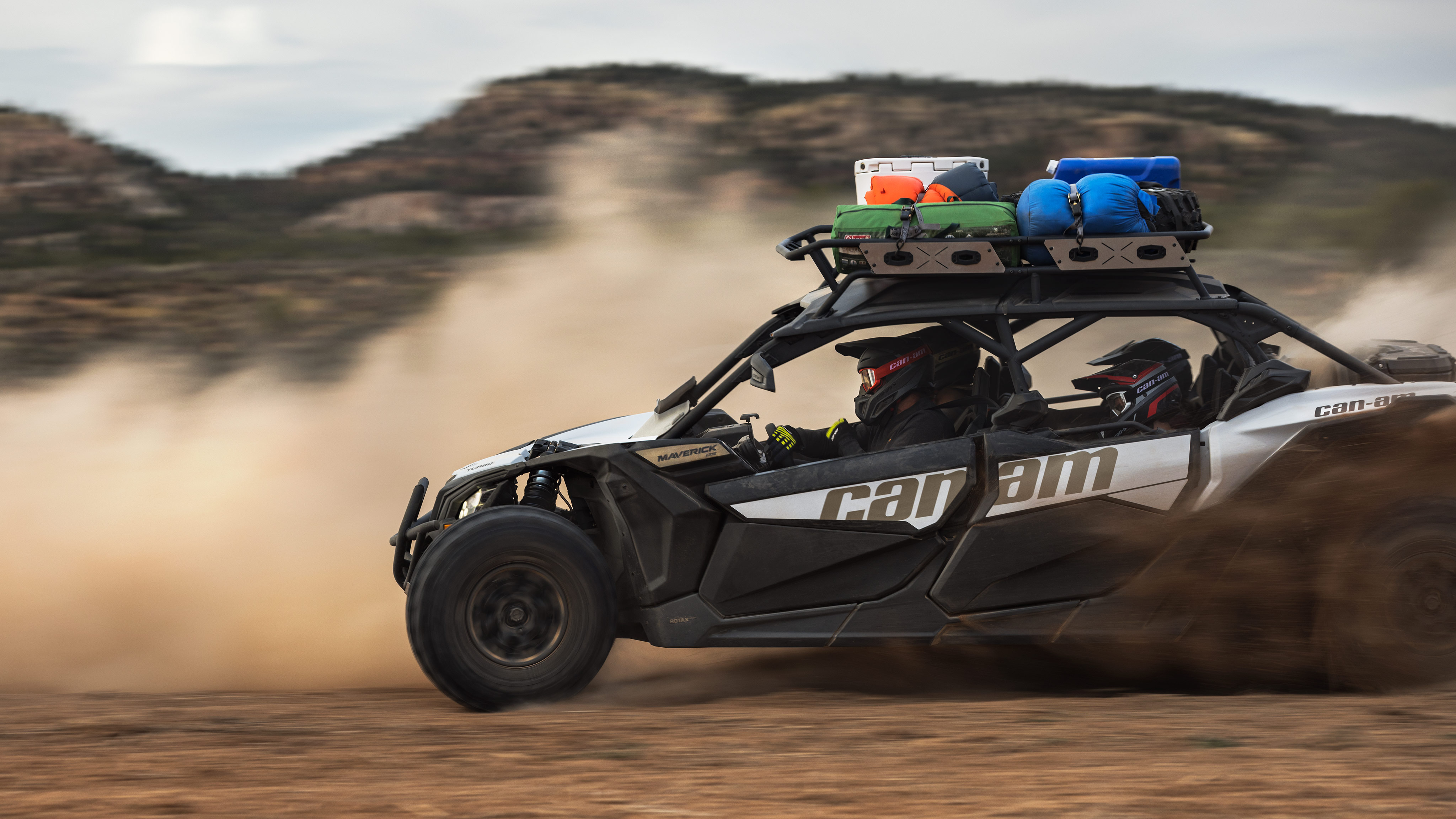 A Can-Am Maverick X3 MAX DS Turbo side-by-side vehicle loaded with gear going at high speed in the desert