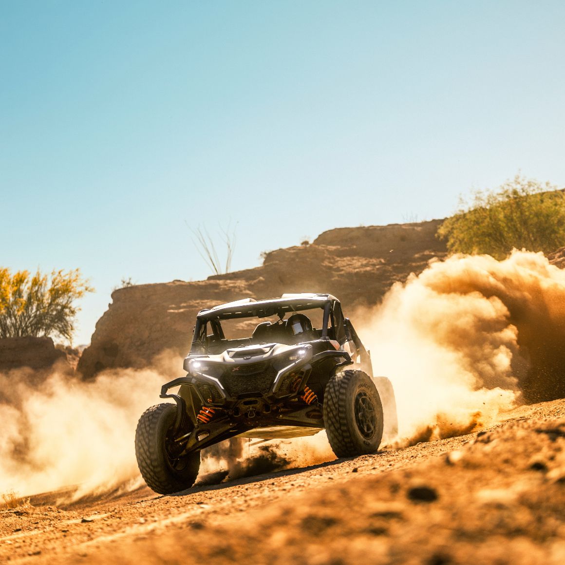 A Can-Am Maverick X RS side-by-side vehicle riding in the desert, leaving a cloud of dust behind
