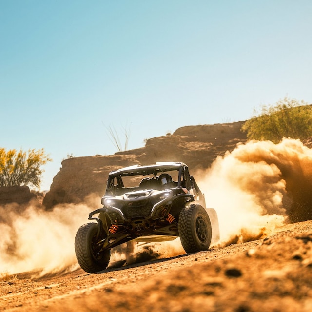 A Can-Am Maverick X RS side-by-side vehicle riding in the desert, leaving a cloud of dust behind