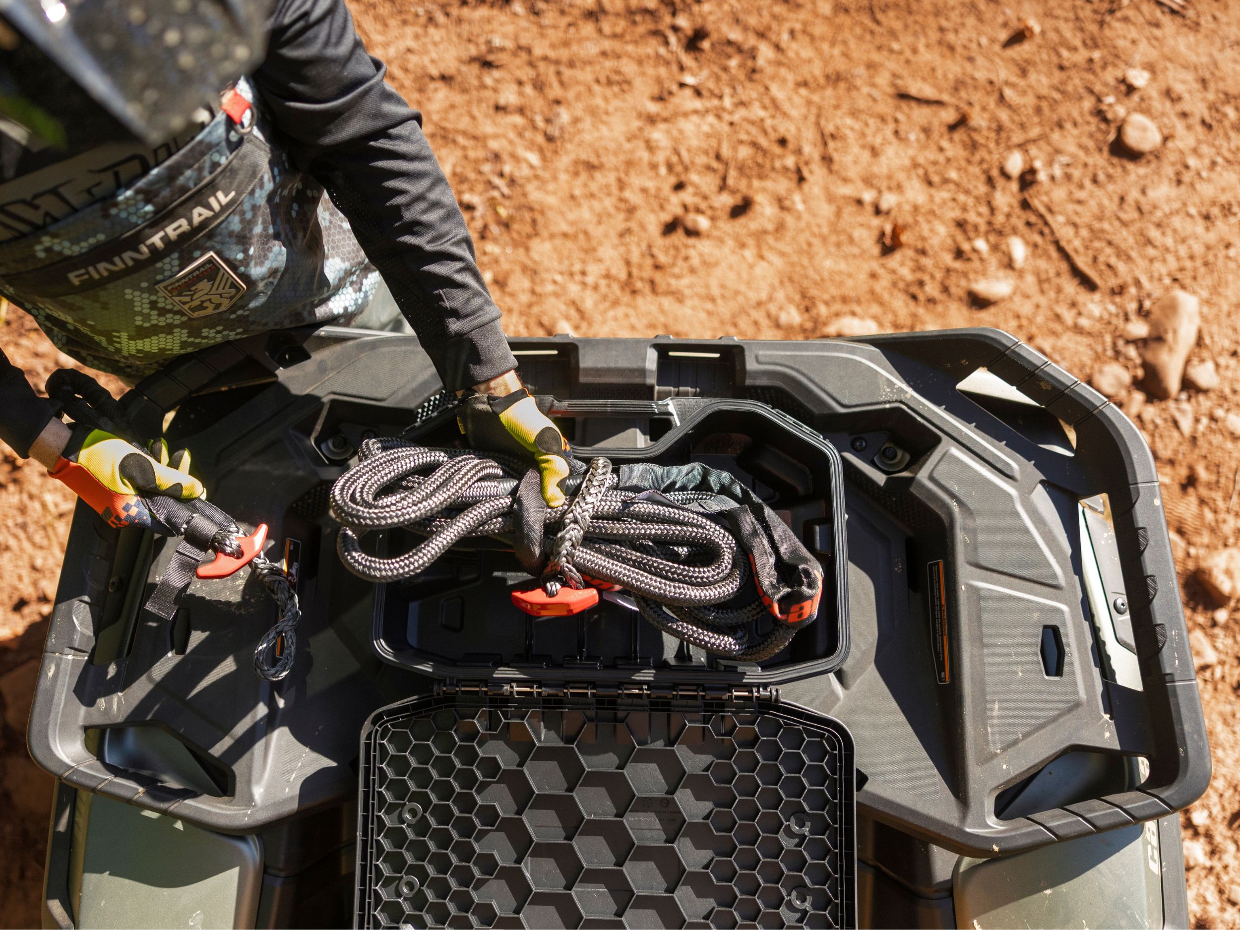 A man storing a rope in a LinQ storage on the front of his Outlander ATV