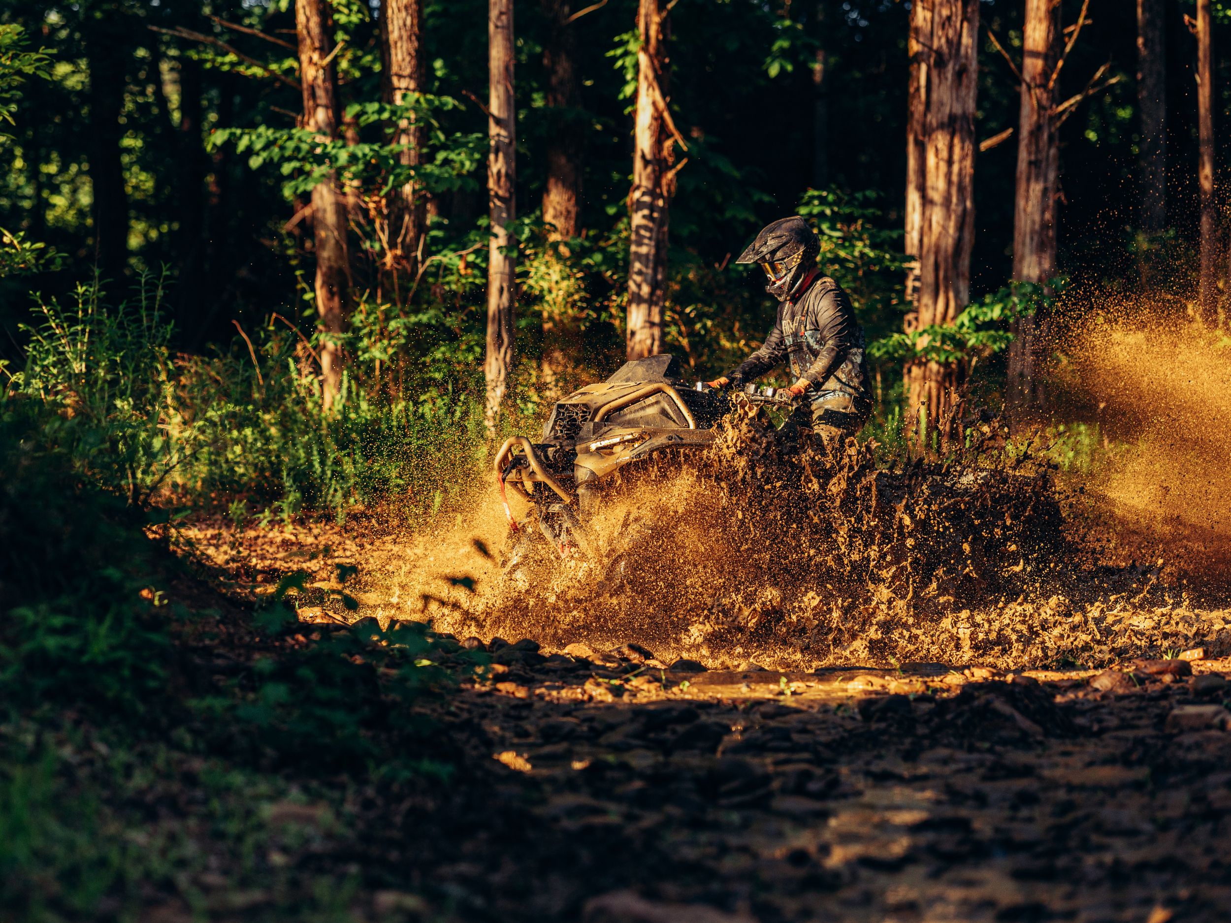 Man riding a Can-Am Outlander ATV, standing up, in deep mud