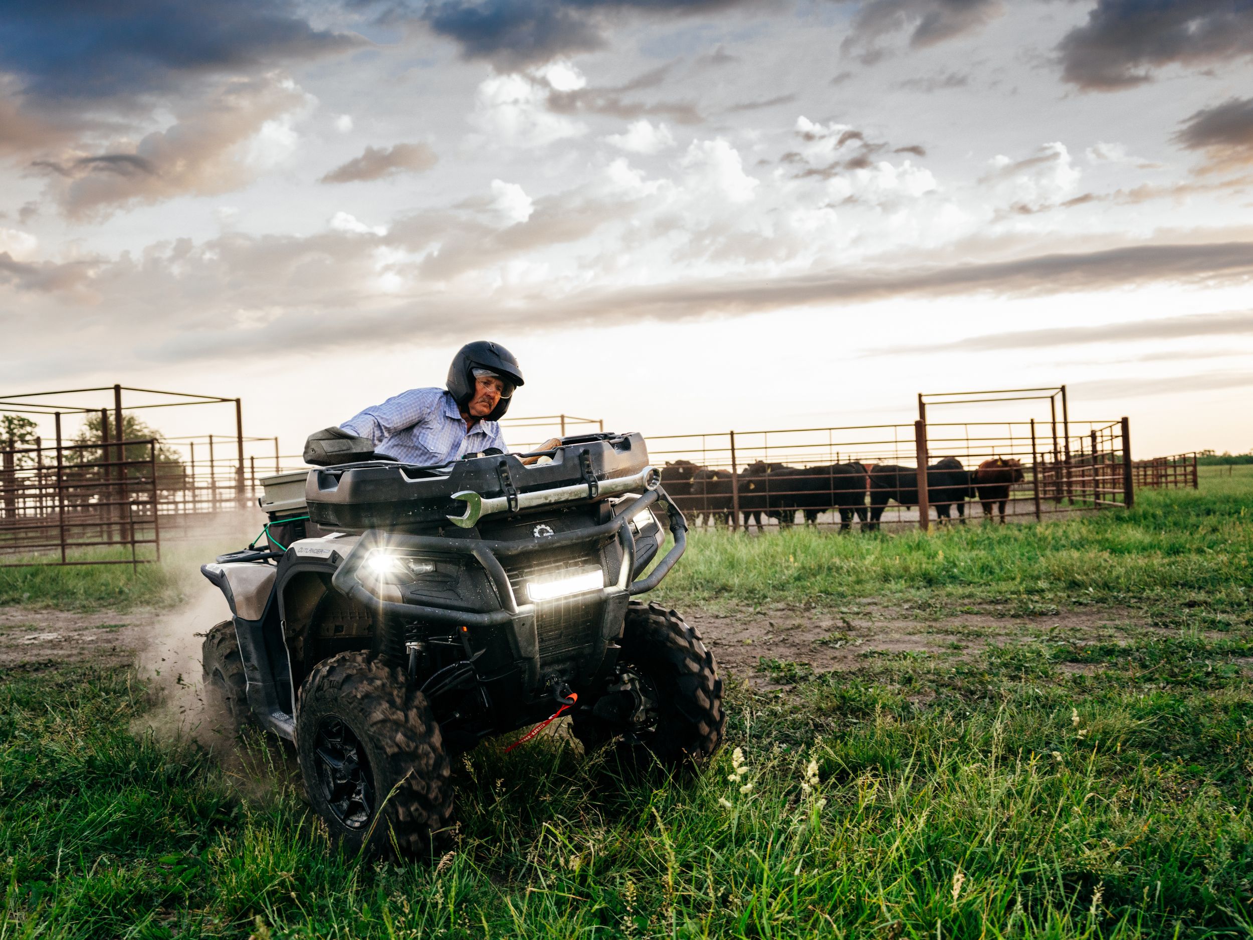 Farmer riding a Can-Am Outlander PRO ATV in a field next to a cattle pen