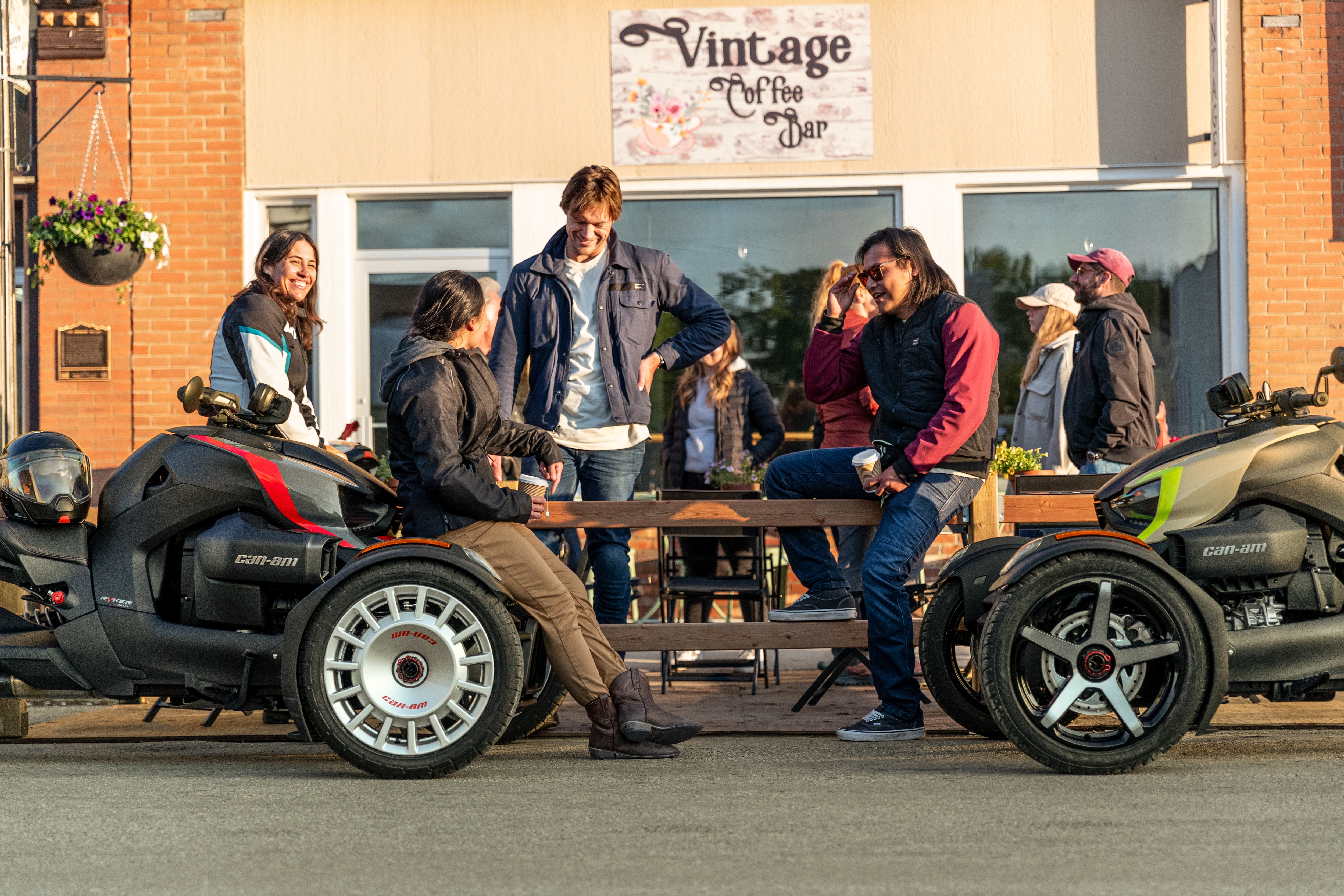 Group of riders chatting next to two 2024 Can-Am Ryker vehicles